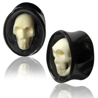 Cargar imagen en el visor de la galería, A pair of black oval Horn Plug Flesh Tunnels with white Totenkopf Bone Inlay, shown on a white reflective surface. Organic expander design for tribal piercing style.
