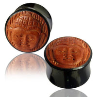 Load image into Gallery viewer, Two Horn Plug Buddha schwarz braun Flesh Tunnel plugs with round wood inlays and carved Buddha design are shown on a white surface, each reflected below.
