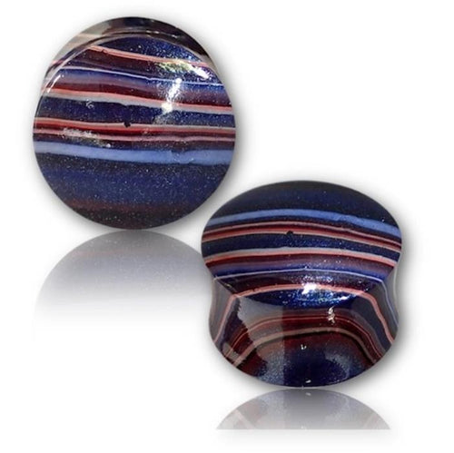 Two hand-painted Holz Plugs in Batik Style (lila, rot, blau) display tribal-inspired horizontal stripes. One stands upright while the other lies on its side, showcasing their glossy finish and organic craftsmanship.