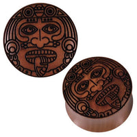Load image into Gallery viewer, The Sawoholz Holz Flesh Plug in brown features a Krieger face engraving with Aztec-style bold lines, wide eyes, nose ornaments, and a protruding tongue. Displayed in top and angled views.
