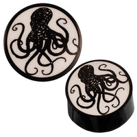 Cargar imagen en el visor de la galería, Schwarz Horn Plug mit glänzend weißem Bone Inlay zeigt ein Tribal Oktopus-Motiv mit detaillierten, geschwungenen Tentakeln auf der Vorderseite.
