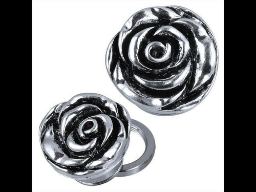 Two metallic, silver-tone Edelstahl Schraub Plug Tunnel Plugs, rose-shaped with dark oxidized detailing. One lies flat while the other is tilted to show a circular back opening and layered, textured petals for a plastic, dimensional effect.