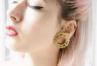 Load image into Gallery viewer, A person with pale pink hair wears bold winged eyeliner, red lipstick, a gold nose ring, and large Brass Tunnel Rauten Bögen antik gold nickelfrei Plug earrings in stretched earlobes. Their eyes are closed, face turned slightly upward.
