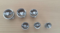 Load image into Gallery viewer, Six Edelstahl Tunnel Plugs Flügel Herz Stein, double flared with faceted stones and winged heart emblems, are arranged by size on a wooden surface.
