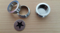Load image into Gallery viewer, An Edelstahl Tunnel Plug Schraubplug Stern schwarz silber Scheibe ribbed Piercing with a black star cutout is placed on a light wooden surface alongside two other metal components.
