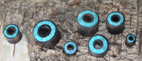 Cargar imagen en el visor de la galería, Seven Flesh Tunnel Eisenholz schwarz Rim Crushed Türkis Inlay ear plugs are displayed on rough tree bark, showcasing their turquoise inlays. The plugs range in size, each featuring striking blue-green accents.
