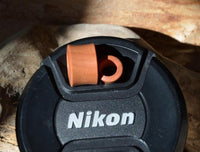 Load image into Gallery viewer, A finely grained, convex red-brown Holz Tunnel aus Rosenholz rests atop a black Nikon camera lens cap on a wooden surface.
