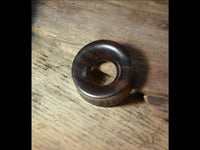 Load image into Gallery viewer, A dark, round Holz Tunnel braun gelb Sonoholz Teakholz double flared with a smooth surface and a central hole rests on a light, textured wooden surface.
