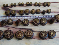 Load image into Gallery viewer, Several Holz Plug Om Blume gold bemalt Lasergravur Kokosholz Inlay Tunnels are arranged by size next to a clear ruler on a wooden surface, neatly organized from small to large in four rows.
