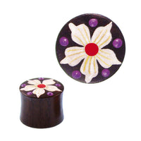 Cargar imagen en el visor de la galería, The Holz Plug braun features a round, dark brown design with a hand-painted white flower with a red center and five petals, accented by purple dots. The Tribal tunnel expander is shown from the side and above.
