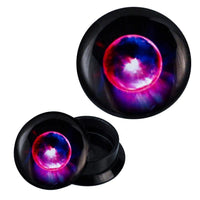 Load image into Gallery viewer, A pair of black Schraub Plug Acryl Komet plugs for all piercings, each featuring a glowing cosmic sphere in red, purple, blue, and white hues—one plug stands upright, the other is shown at an angle.
