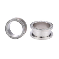 Load image into Gallery viewer, Two silber Tunnel Plug Schraubplug Chirurgenstahl Edelstahl mit schmalem silbernen Glitzer Rand liegen auf weißem Hintergrund – einer steht aufrecht, der andere liegt seitlich.
