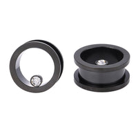 Load image into Gallery viewer, Zwei schwarze Edelstahl Flesh Tunnel ribbed Plugs mit Glitzer-Zirkonia Stein: Einer steht aufrecht und zeigt den hohlen Kern, der andere liegt flach und präsentiert den funkelnden Stein am Rand.
