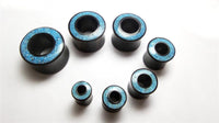 Cargar imagen en el visor de la galería, Seven black cylindrical plugs featuring blue-patterned tops, including the Flesh Tunnel Eisenholz schwarz Rim Crushed Türkis Inlay, are arranged on a white surface in descending size order, forming a gentle arc.
