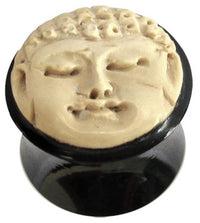 Load image into Gallery viewer, The Bio Horn Plug Buddha schwarz hell Flesh Tunnel Holz is a round black horn plug topped with a carved ivory-toned Buddha face in a calm, serene expression and closed eyes.
