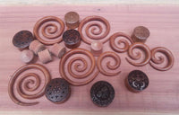 Load image into Gallery viewer, A selection of Sawoholz Plug braun Tunnel Expander Mandala schwarz, featuring intricate mandala and geometric engravings, displayed on a smooth wooden surface.
