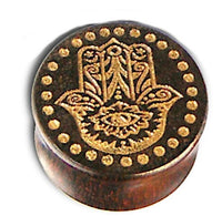 Load image into Gallery viewer, A round Holz Plug named &quot;Poor Mans Hand&quot; is crafted from Tamarind wood, laser-engraved with a gold-painted Khamsa (Fatima hand) design featuring an eye and surrounded by a ring of gold dots in a tribal style.
