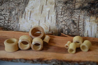 Cargar imagen en el visor de la galería, A light-colored, smooth Holz Flesh Tunnel made of Krokodilholz with a slightly convex, double-flared shape is displayed on rough, natural wood with a rustic bark and tree background.
