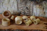 Cargar imagen en el visor de la galería, Several Holz Flesh Tunnel Krokodilholz hell leicht konvex double flared plugs in different sizes are scattered on rough wood, with a textured tree bark background.
