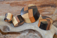 Cargar imagen en el visor de la galería, Four laminiert Holzplug vier Farben Muster Tribal Holz Plugs, each handmade with interlocking dark and light wood patterns, are arranged on textured driftwood, set against a blurred wooden background.
