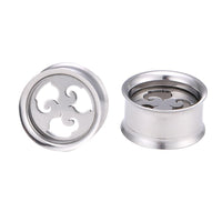 Load image into Gallery viewer, Two Schraubplug Tunnel Edelstahl silber with geschwungenes Muster, featuring decorative cut-out designs on the front, are displayed on a white background—one standing upright, the other lying on its side.
